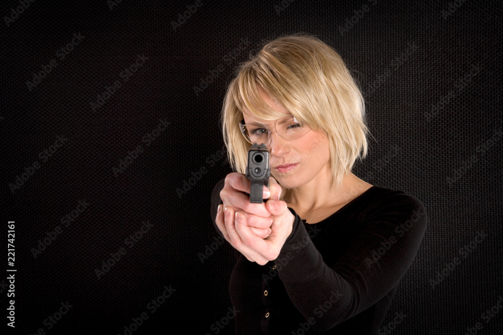 A blonde adult woman aiming a handgun isolated on black. A blonde adult woman aiming a handgun isolated on black.