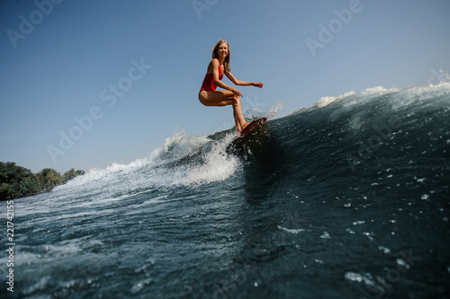 High blue wave on a foreground and beautiful blonde woman wakesurfing on board