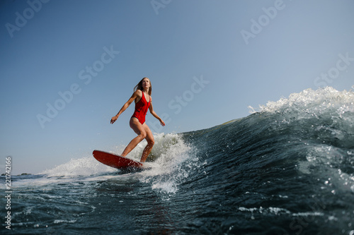 Beautiful slim woman wakesurfing on a high blue wave