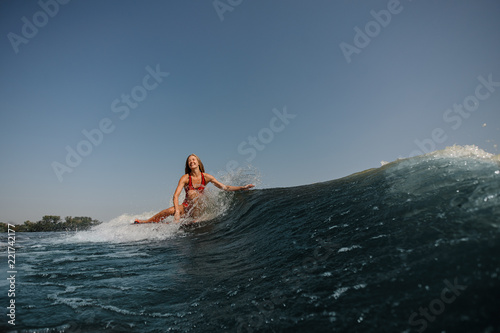 Beautiful smiling woman wakesurfing on a high blue wave