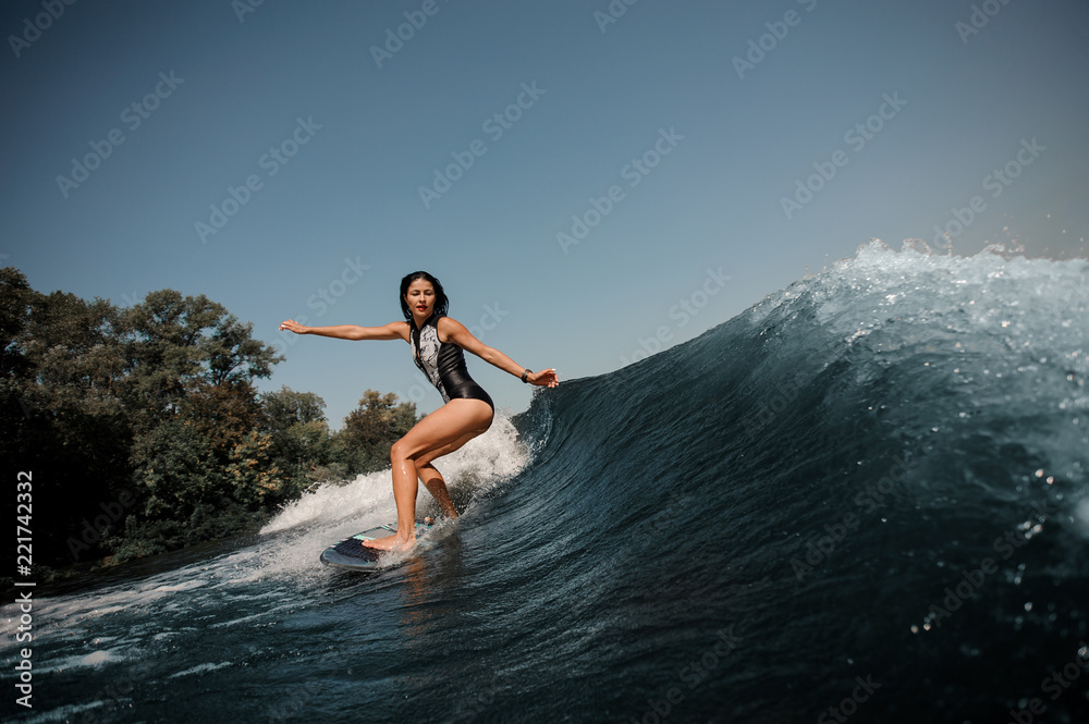 Sexy slim brunette woman wakesurfing on board down the blue water