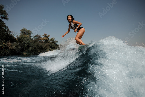 Sexy young brunette woman wakesurfing on board down the blue water