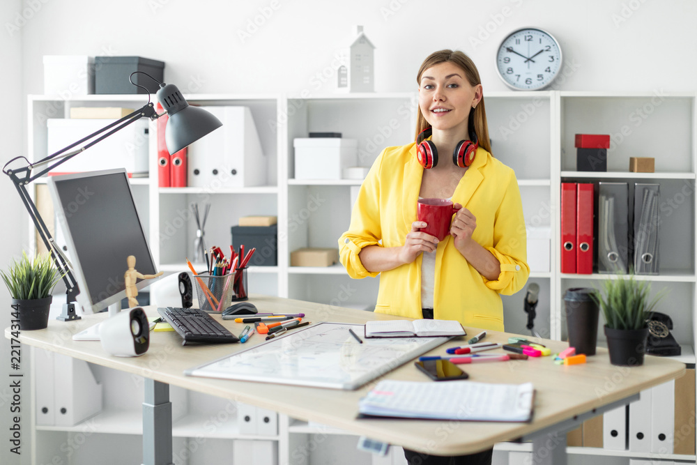 A young girl in headphones stands near a table with a red mug in her hands. Before the girl on the table is a magnetic board A young girl in headphones stands near a table with a red mug in her hands. Before the girl on the table is a magnetic board
