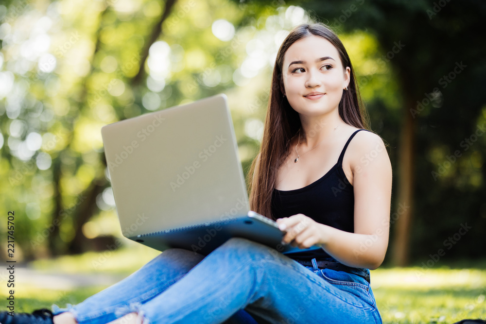 Japanese student working on her laptop while laying on grass on green background Japanese student working on her laptop while laying on grass on green background