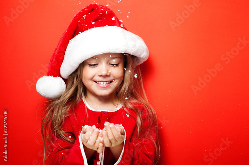 Happy smiling funny girl in Christmas cap under the snow on the red background. Merry Christmas. Sale. Black Friday. Discount