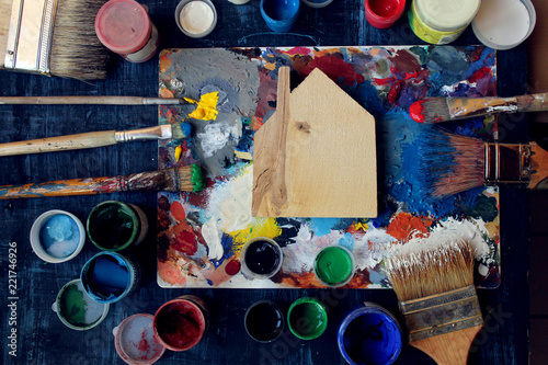  a miniature wooden house lies on a palette surrounded by brushes and paint cans