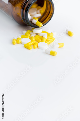 Close up of assorted medication capsules spilling from bottle over white background, copy space photo