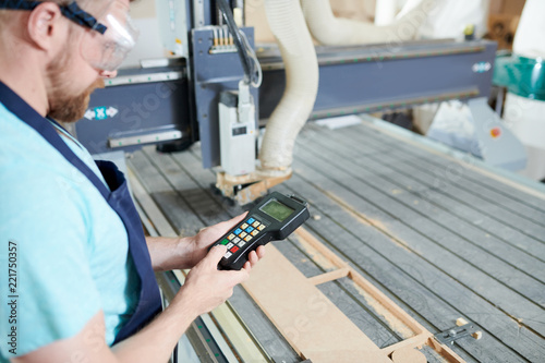 Operator controlling the work of machine with console in carpentry shop