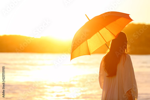 Woman with umbrella at sunset on the beach