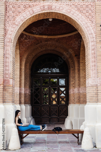 Young asian student on university campus with computer laptop on bench outdoors © dianagrytsku