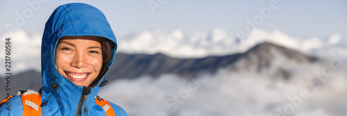 Hiking hiker woman portrait in mountain summit snow capped peaks in sunrise above clouds panoramic banner. Asian girl smiling trekking in mountains.