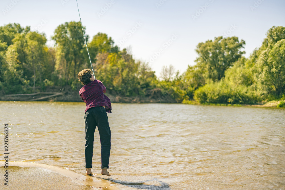 young teenager fisherman in casual catching fish on the river bank with rod on a summer day d young teenager fisherman in casual catching fish on the river bank with rod on a summer day d