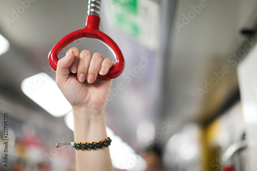 female hand holding a looped handle in urban public transportation (local subway, underground) with blurred background