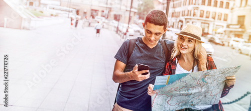 Casual young man and woman with map using phone on street exploring city while traveling