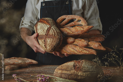 Baker in black apron holds variety of bread photo