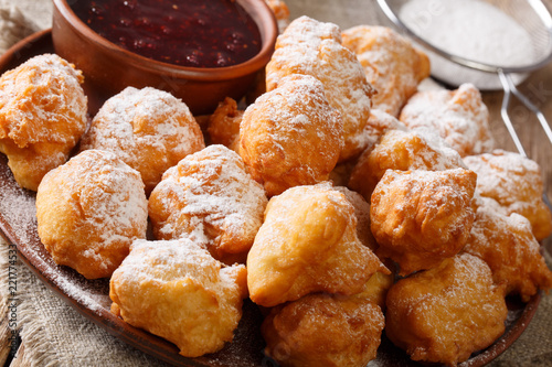 Delicious fried donuts are served with raspberry jam and powdered sugar close-up on a plate. horizontal