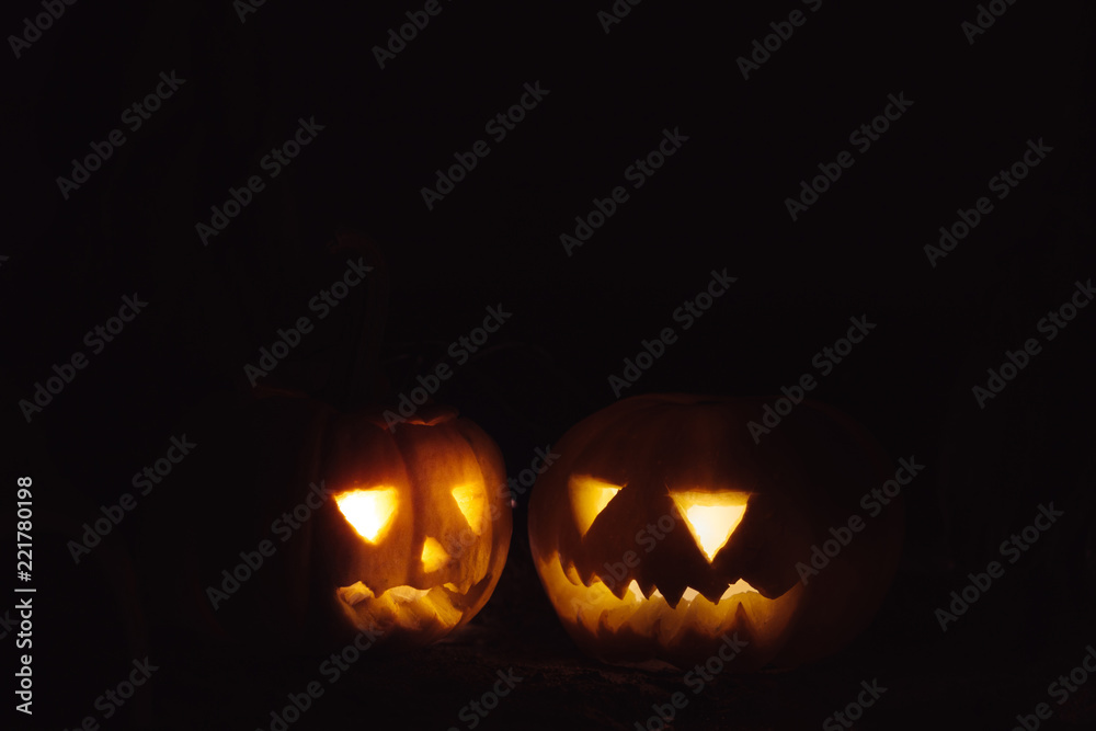 Spooky and laughing carved Halloween Jack-o-lantern pumpkins with lights isolated over dark background - with copy space. Spooky and laughing carved Halloween Jack-o-lantern pumpkins with lights isolated over dark background - with copy space.