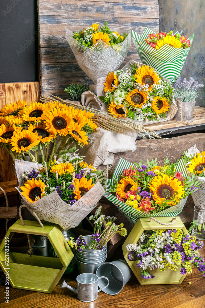 Fototapeta premium Workplace florist. Beautiful bouquets with sunflowers on a wooden table. vertical shot