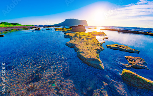 First sunrays at sunrise at Ilchulbong volcano crater with view over ocean and green moss stones , Jeju Island, South Korea. photo