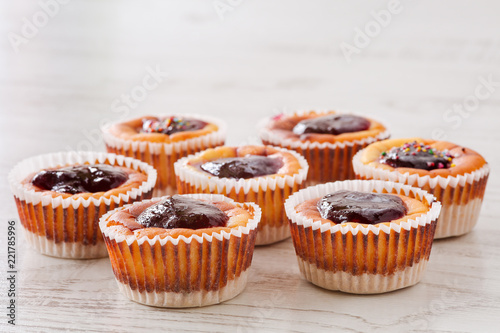 Seven delicious, homemade mini cheesecakes with berry jam in muffin cups on a wooden table