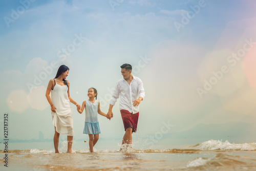 Happy asian family - father, mother, kid hold hands and run together with fun along daylight sea beach. Travel, active lifestyle, parents with children on tropical summer vacations.