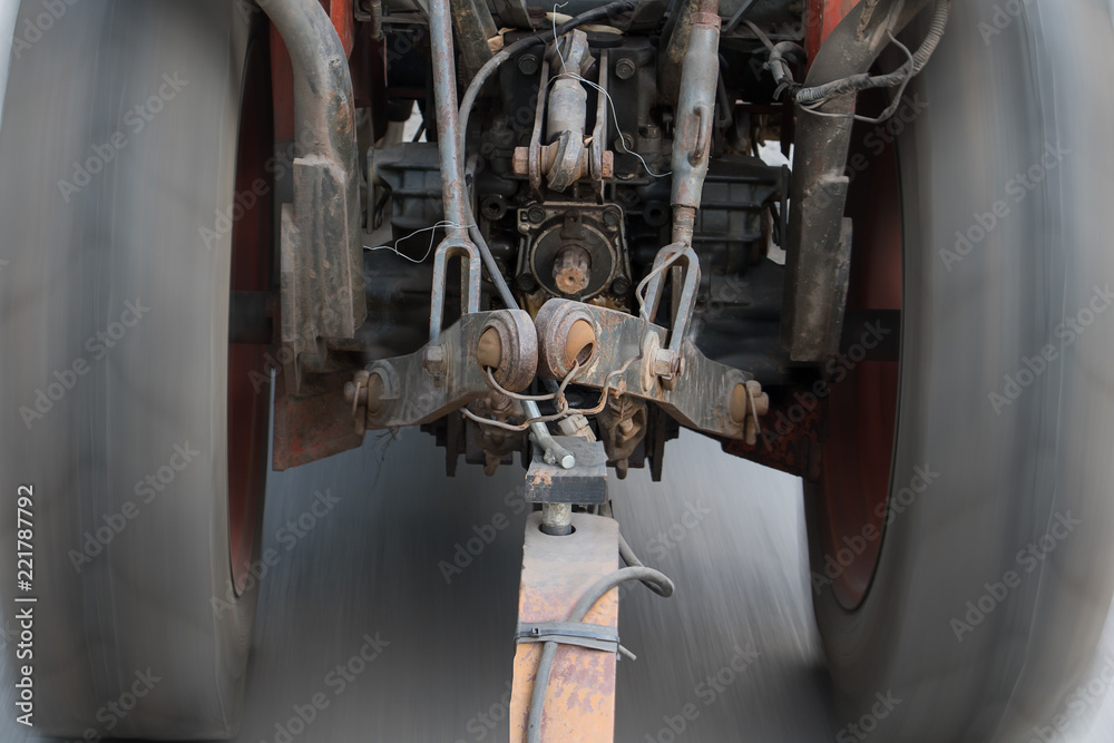 Fototapeta premium An old tractor ride on asphalt road and pulls a load with rod.