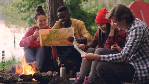 Cinemagraph loop - male and female friends tourists are sitting around fire and studying maps during hike in forest in summer. People are wearing casual clothing. photo