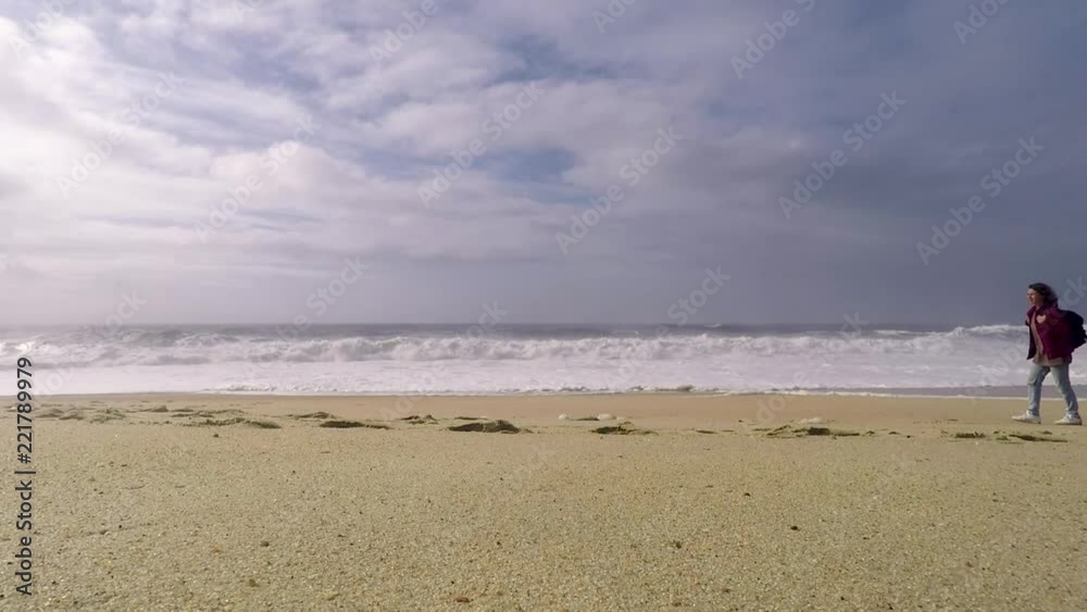 A young woman is walking on the ocean North Beach in Nazare, Portugal. Woman-traveler with a backpack. A young woman is walking on the ocean North Beach in Nazare, Portugal. Woman-traveler with a backpack.