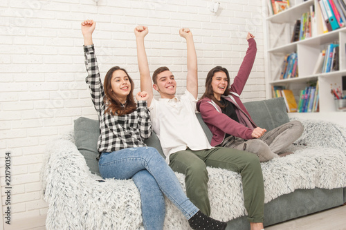 Three teenage fans are sitting on the couch and watching TV