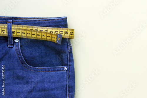 yellow measure tape in jeans on background, concept of weight loss, copy space