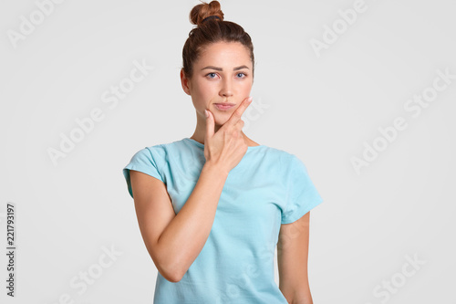 Thoughtful puzzled woman with hesitant expression, holds chin, dressed in casual clothes, ponders on something, isolated over white background. Student being deep in thoughts. Hesitation concept © sementsova321