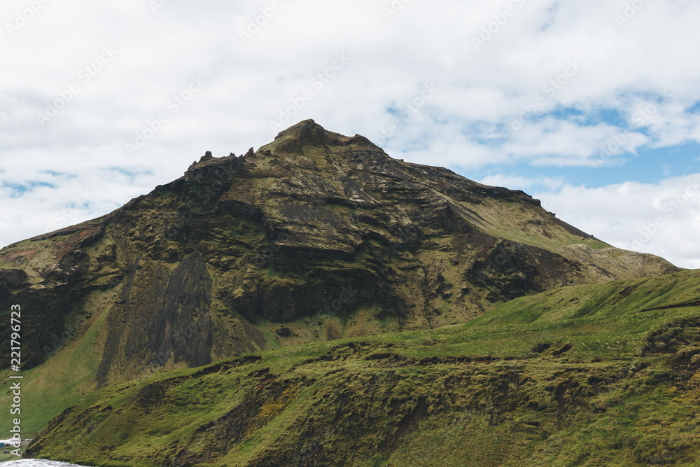 scenic view of landscape with mountain under cloudy blue sky in Iceland scenic view of landscape with mountain under cloudy blue sky in Iceland