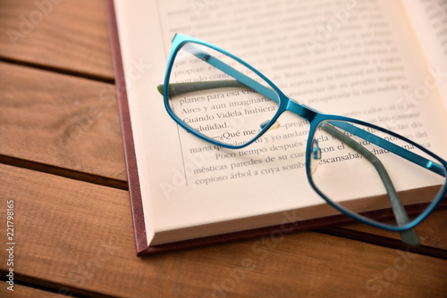 Blue eyeglasses on open book on wood table top