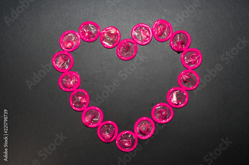 The heart is laid out with pink condoms on a black background