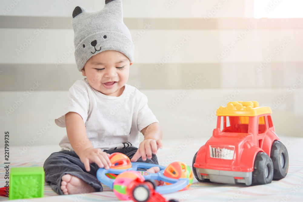 kid boy toddler playing with toy on bedroom at home.Happy laughing baby wearing bubble hat sitting on parents bed kid boy toddler playing with toy on bedroom at home.Happy laughing baby wearing bubble hat sitting on parents bed