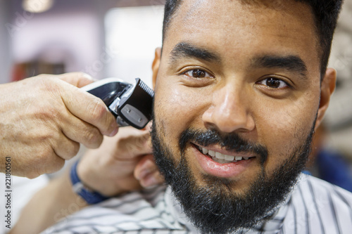 Young black man in a barbershop. Portrait of diverse POC model posing in a barber chair with a smile. Happy customer in a male beauty salon receiving a new haircut