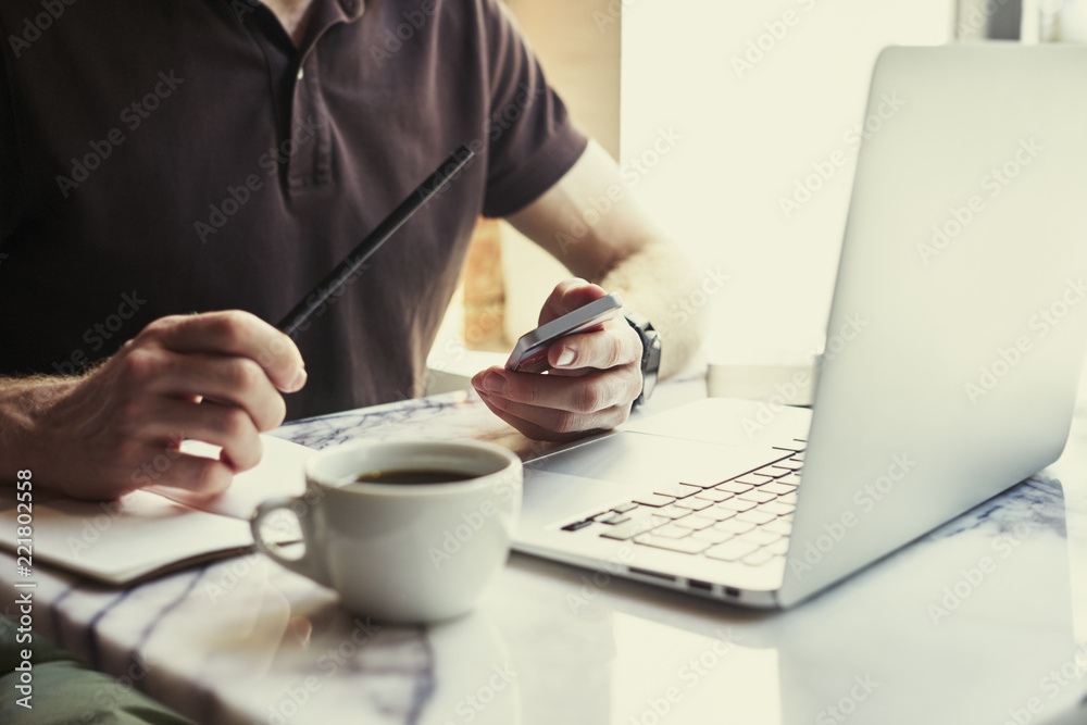 Man writing in notebook using laptop while sitting in cafe having coffee. Concept of young business people working in public space or co-working. Man writing in notebook using laptop while sitting in cafe having coffee. Concept of young business people working in public space or co-working.