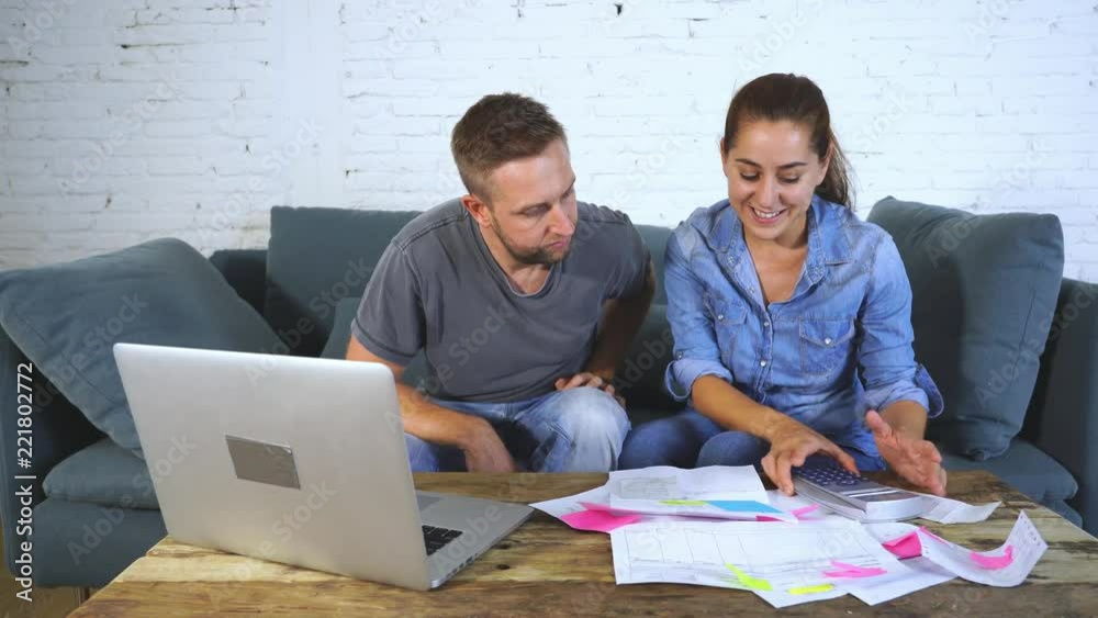 Happy young couple paying bills together and managing budget, sitting on the sofa and using calculator and laptop in financial concept Happy young couple paying bills together and managing budget, sitting on the sofa and using calculator and laptop in financial concept