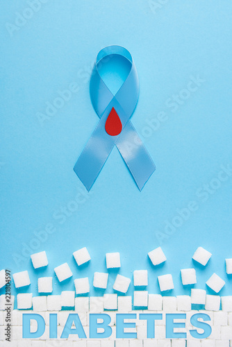 inscription diabetes blue ribbon awareness with red blood drop and ruined wall made of sugar cubes on a blue background