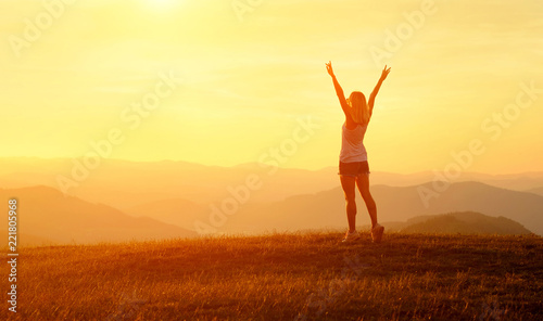 Happy woman with open arms stay on the peak of the mountain 