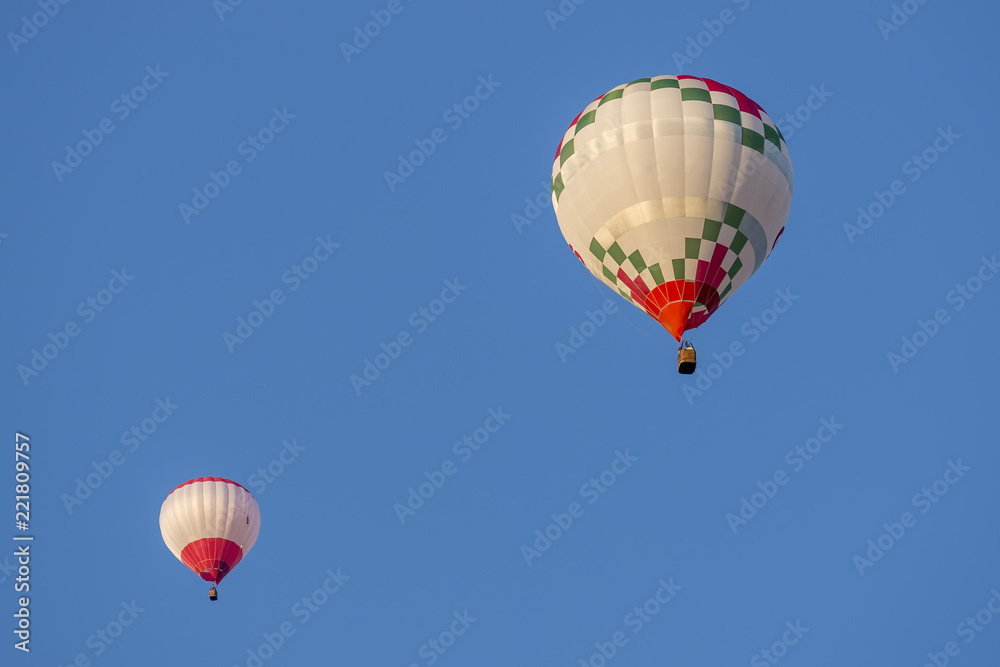 Fototapeta premium Pair of hot-air balloons lit by the light of the sunset against a beautiful blue sky