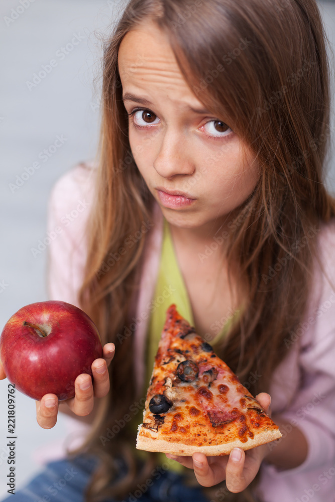 Young teenager girl cannot decide between appetizing pizza and healthy apple Young teenager girl cannot decide between appetizing pizza and healthy apple