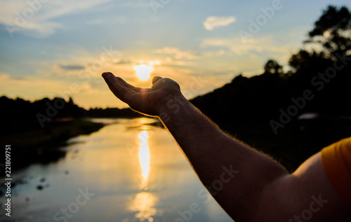 Capture moment to admire sunset nature beauty. Enjoy sunset above river surface. River sun reflection. Catch last sunbeam. Male hand pointing at sun in blue sky at evening time admire landscape