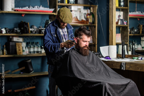 Hipster client getting haircut. Barber with hair clipper works on haircut of bearded guy barbershop background. Barber with clipper trimming hair on nape of client. Hipster hairstyle concept