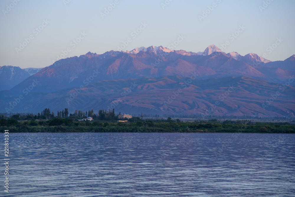 View of the lake and mountains during sunset, which creates purple shadows.