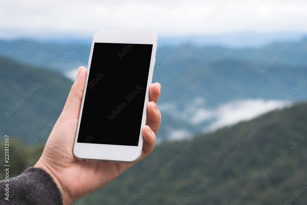 Mockup image of a hand holding and showing white smart phone with blank desktop screen in outdoor with blur green mountains background Mockup image of a hand holding and showing white smart phone with blank desktop screen in outdoor with blur green mountains background