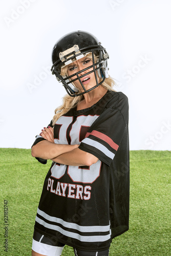 angry young woman in american football uniform looking at camera with crossed arms isolated on white