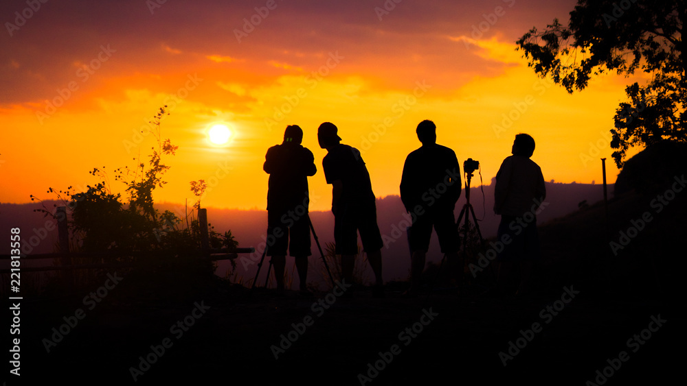 Silhouette of group of friends standing and watching sunset on mountain in evening.