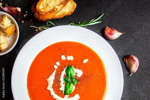 Tomato Soup with herbs on black slate table. Fresh homemade cream of Tomatoes soup with a swirl of cream. Top view.