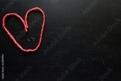 Red heart on a black background. Figure woolen thread on a wooden board with an empty space for text. The concept of needlework, knitting.